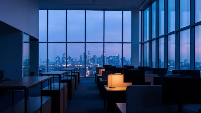 An empty top-floor office at dusk, one desk lamp lit against a city skyline through floor-to-ceiling glass.